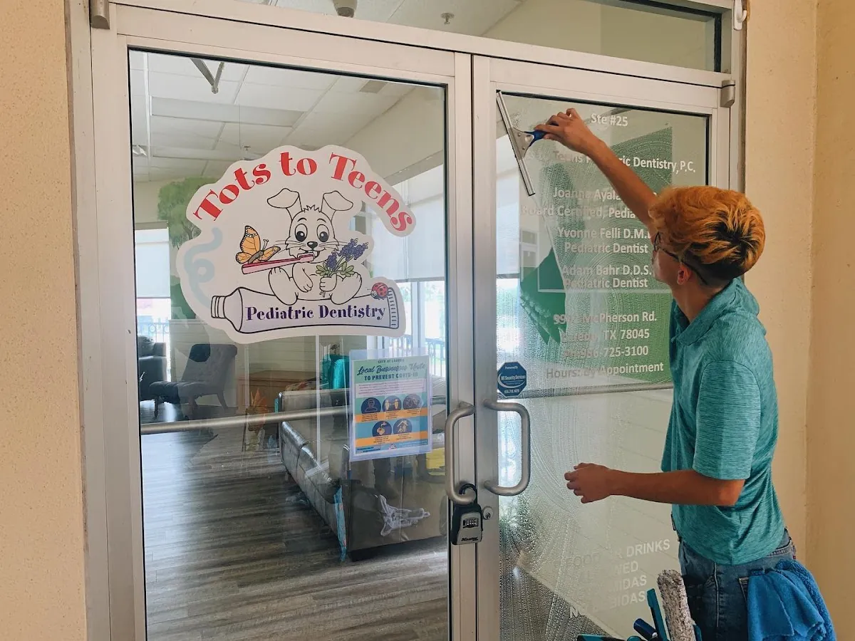 Otto's technician cleaning the entrance windows of a Laredo storefront